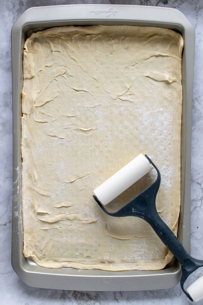 the raw puff pastry is shown in the baking sheet with rolling pin on top